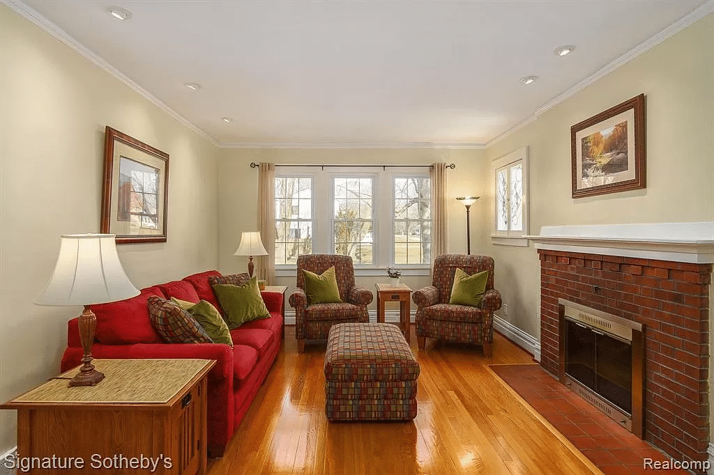 A living room with wooden floors, sofa chairs, and a brick fireplace.